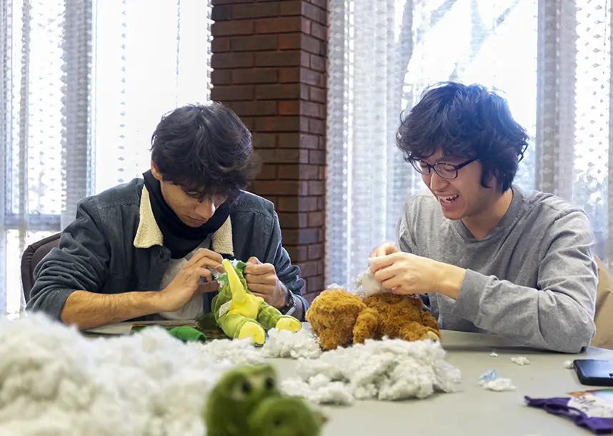 Two students sit at a table while assembly stuffed animals