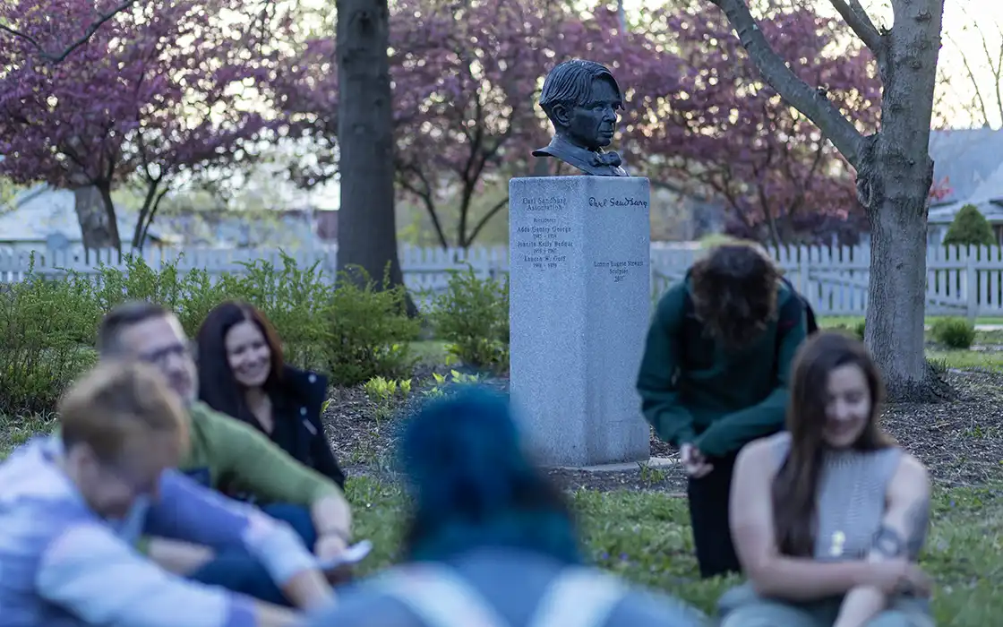 A group of students and faculty sit outside on the grass.
