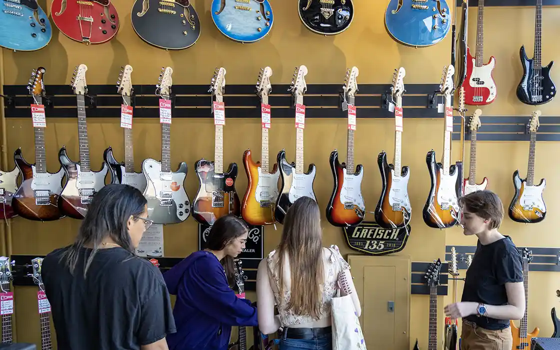 A group of students are inside a store looking at a wall of guitars.
