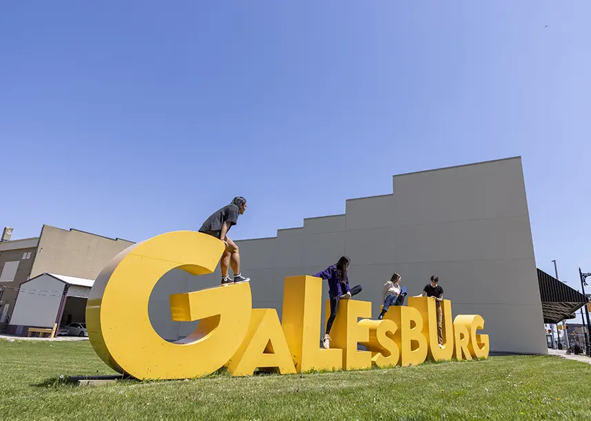 A group of students climbs on a large 3d sign that says Galesburg