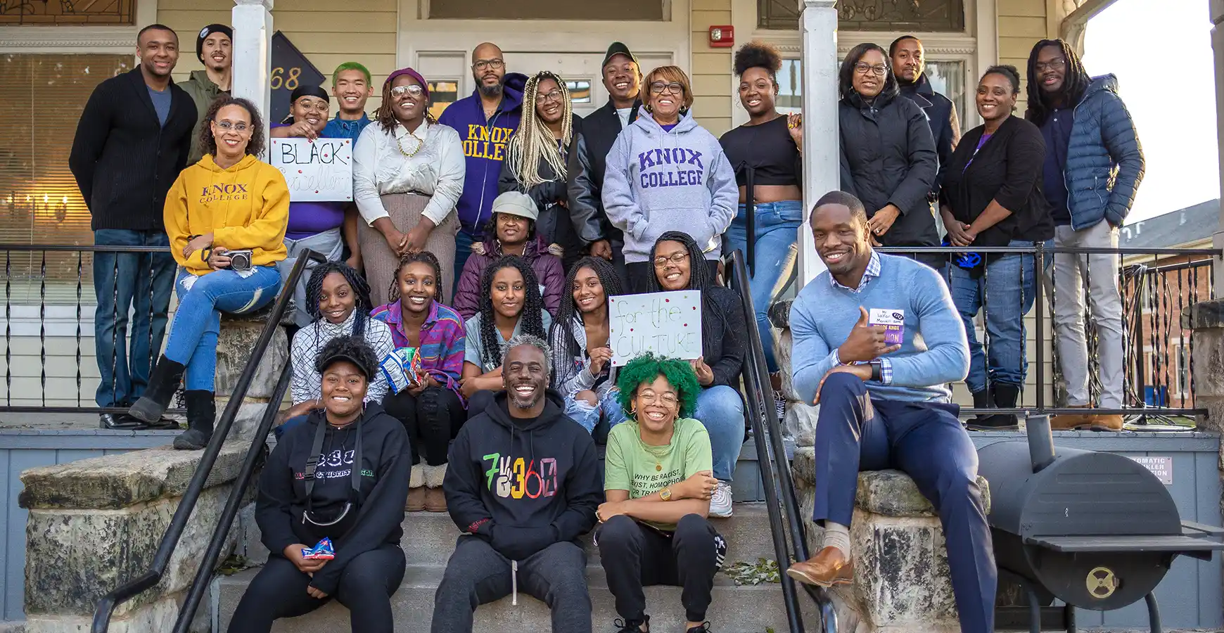 ABLE alumni and students stand on the front steps of ABLE house and smile for a photo.