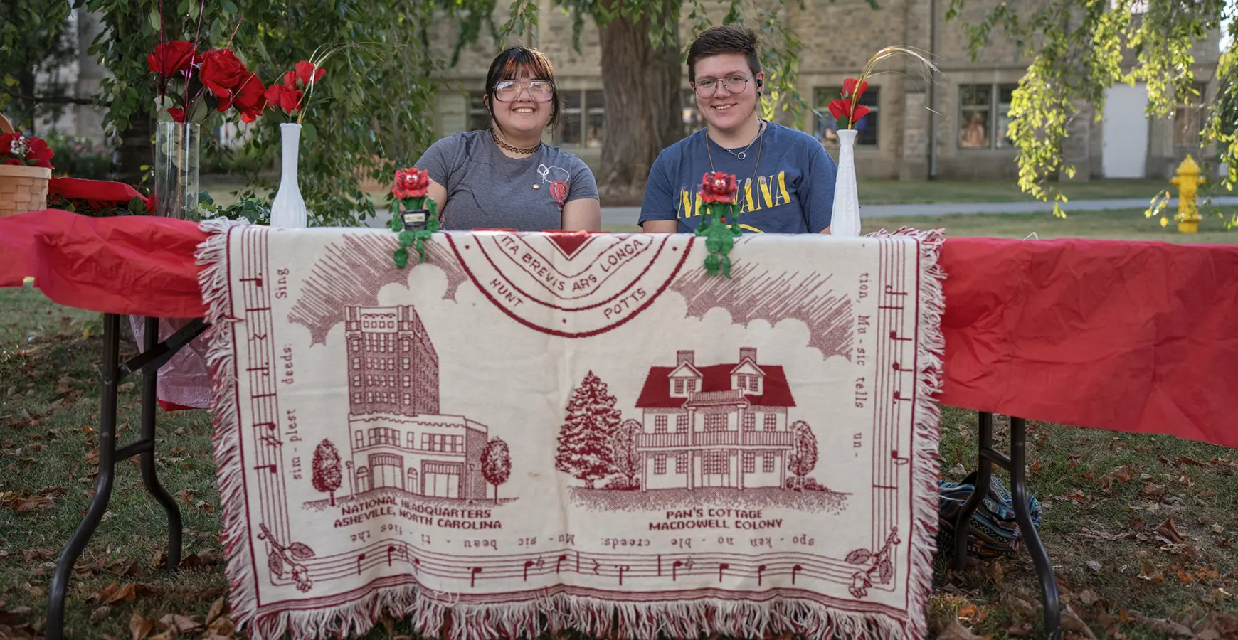 Two students sit at a table with a quilt hanging over the table.