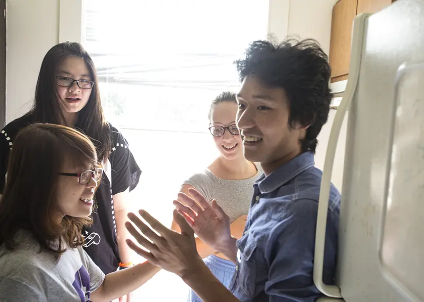 A group of students talk while standing in a kitchen.