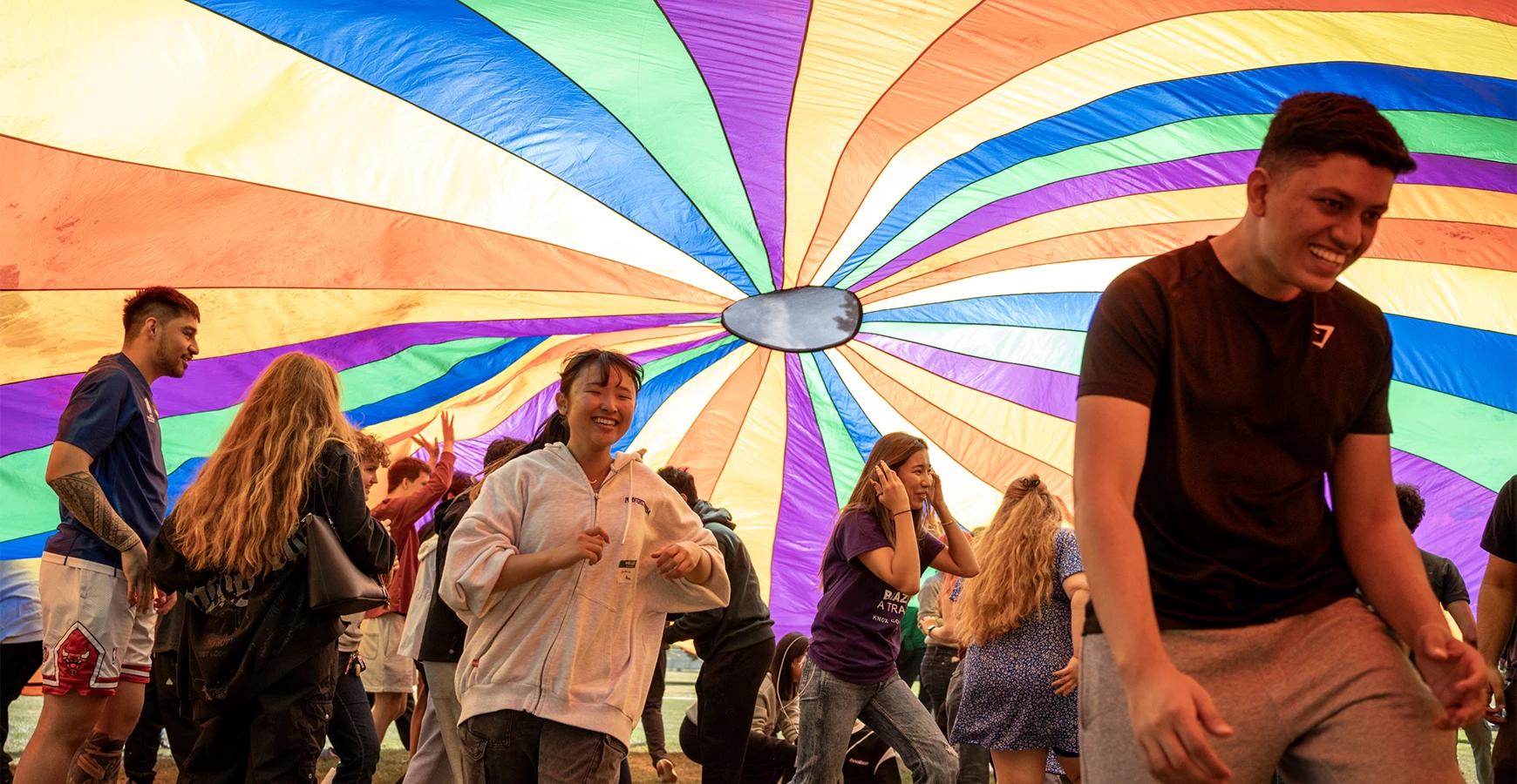 Students walk under a rainbow parachute.