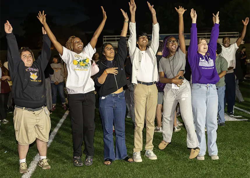 A group of students stand in a line with their hands in the air.