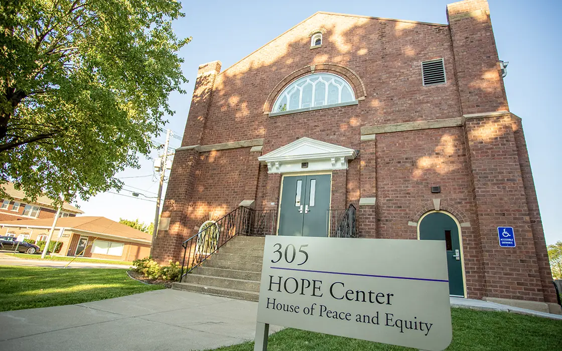 The brick HOPE Center is pictured. Its unique, stained glass half-circle window is visible above the entry, along with a sign that says HOPE Center—House of Peace and Equity.