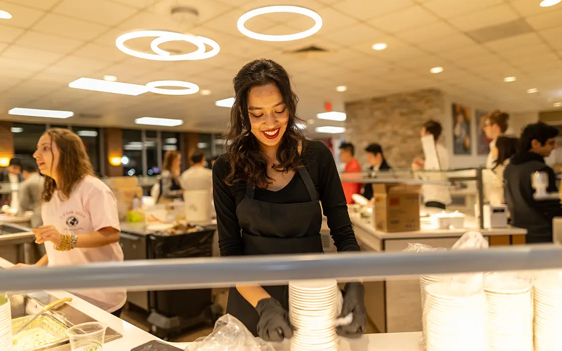 A student worker stack dishes while standing behind a counter in the Hard Knox Cafe.