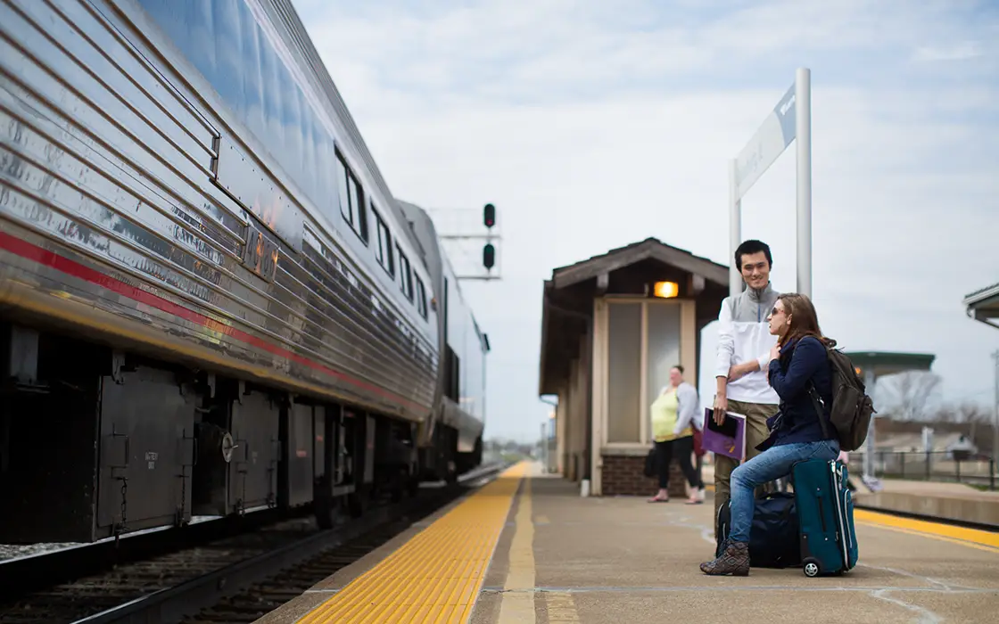 A student waits on the Galesburg train platform as an arriving train comes to s sto. 