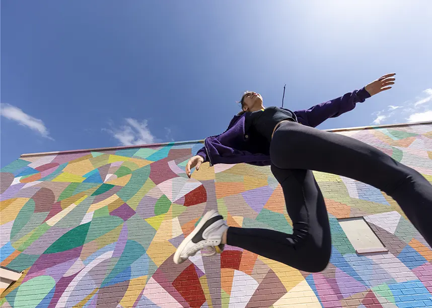 A Knox student striding in front of a building with a multicolored mural.