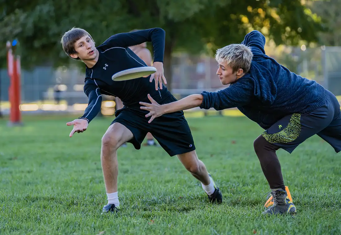 Two students play with a frisbee outside.