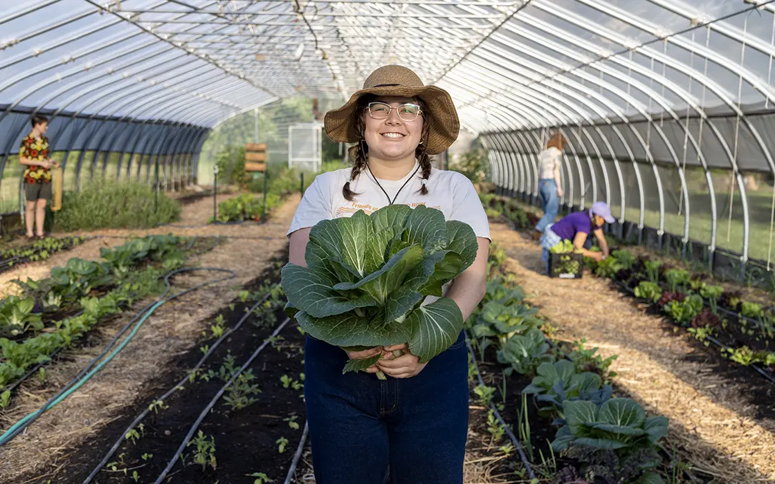 A student stands in a field holding a large vegetable.