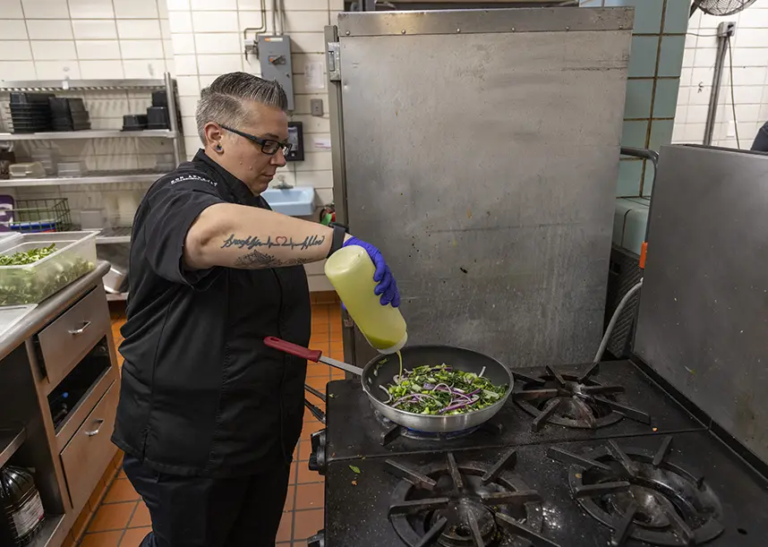 A chef works in the kitchen, cooking a meal on the stove.