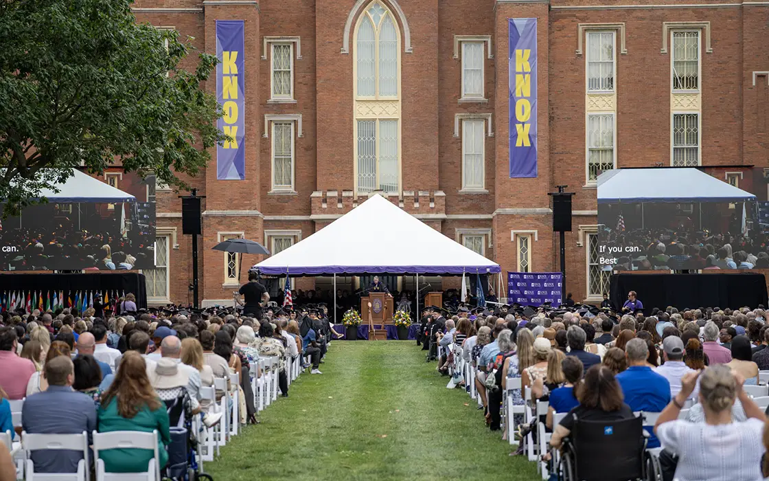 Crowds sit in chairs on the south lawn of Old Main. A tent is set up at the front of the crowd.