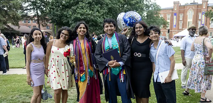A group of graduates and family members pose together. Old Main is visible in the background.