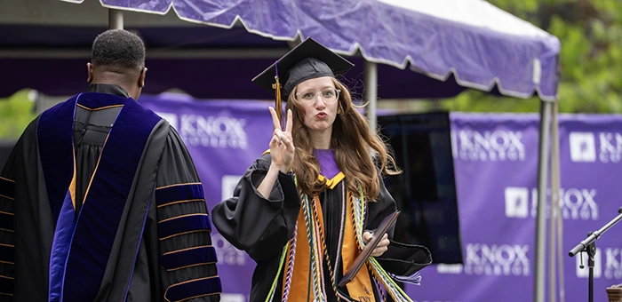 A graduate gives a peace sign to the camera after having received her diploma on stage.