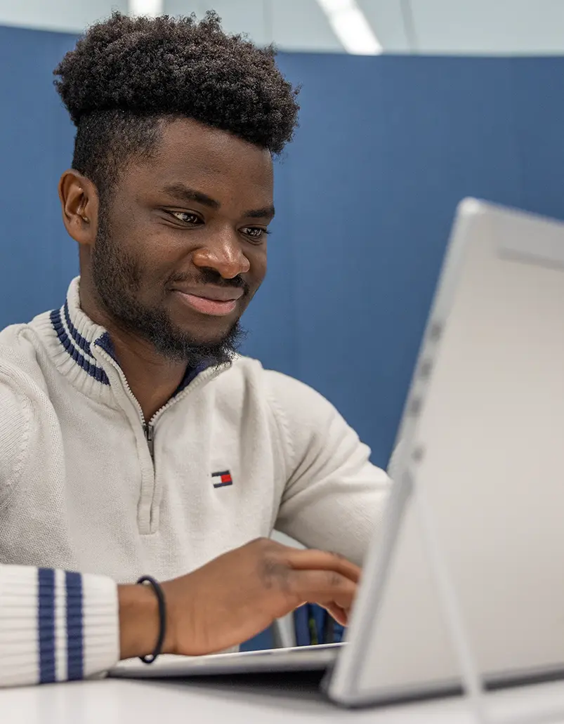 A student smiles as he works on his laptop computer. 