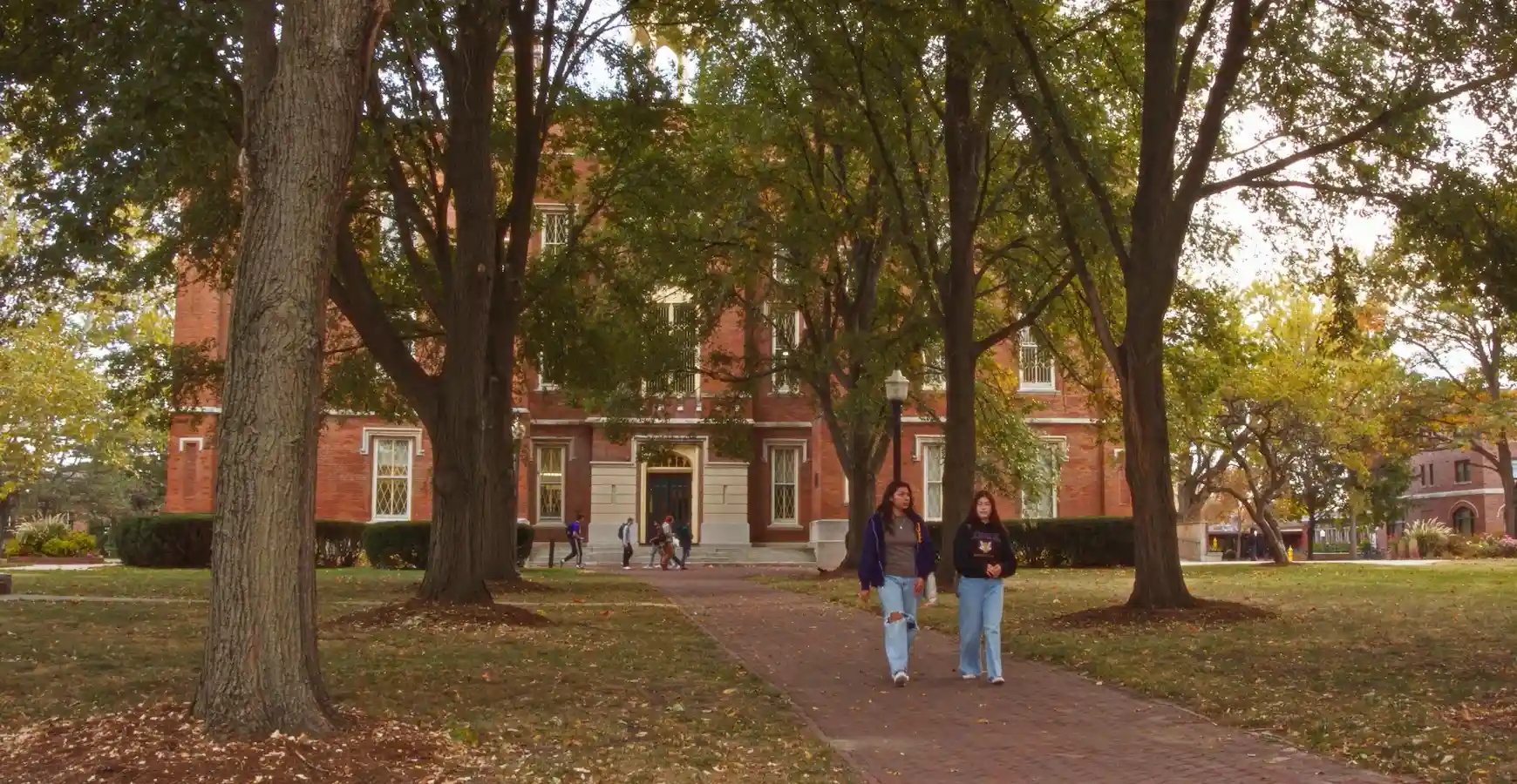Students walk on a tree-covered brick path leading away from Old Main. 