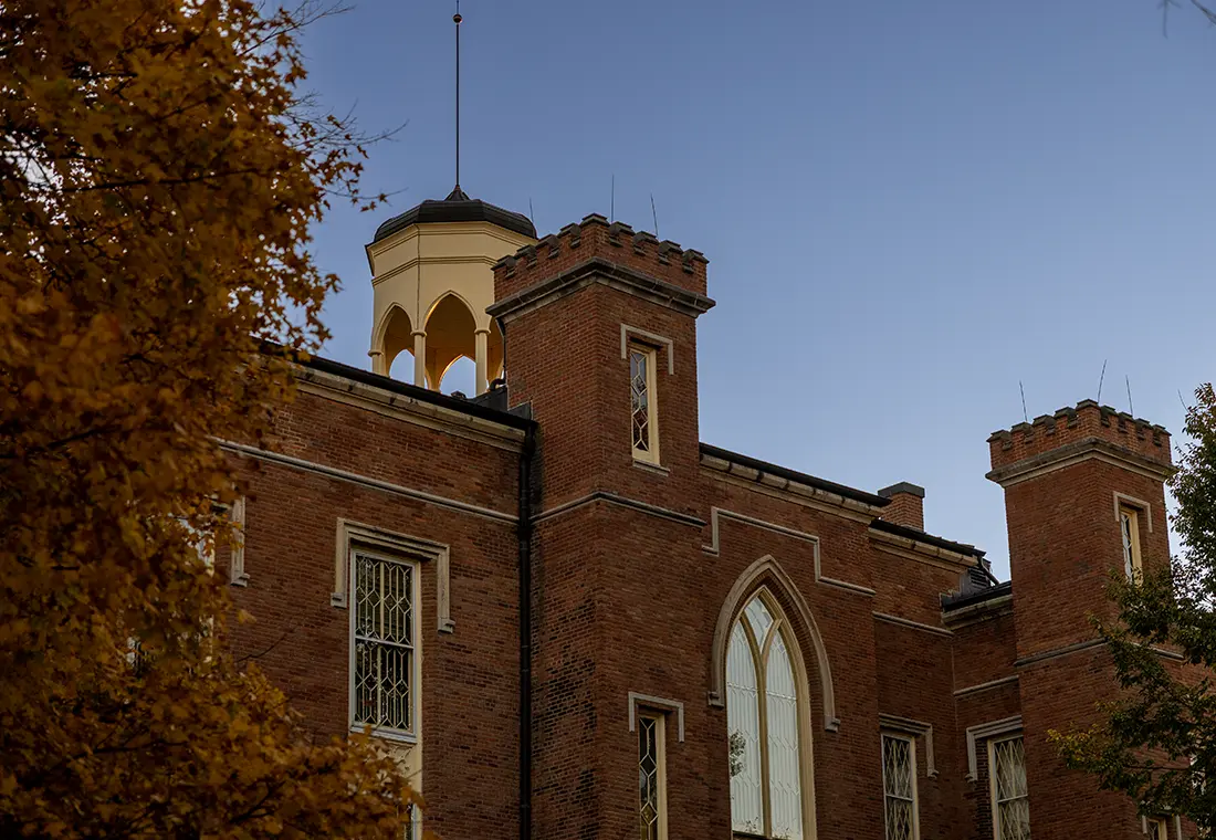 Knox College's Old Main flanked by fall trees and a blue sky.