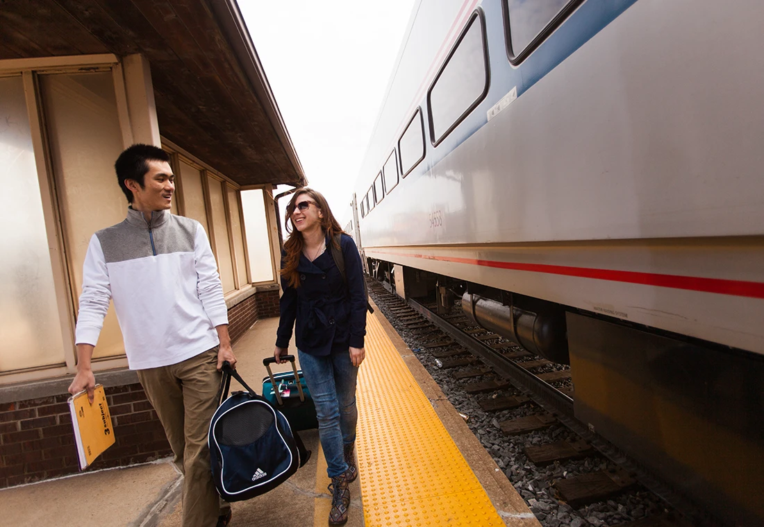 Two students walk on a train station platform as an Amtrak train arrives.