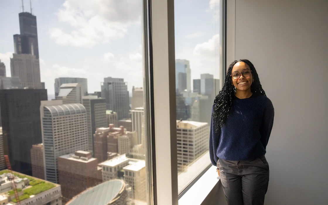 A Knox student in business attire stands at a window overlooking the Chicago skyline.