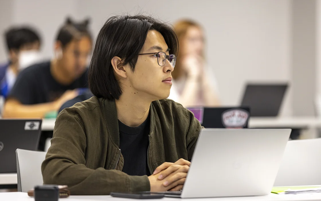 A Knox student with a laptop looks to the front of classroom.