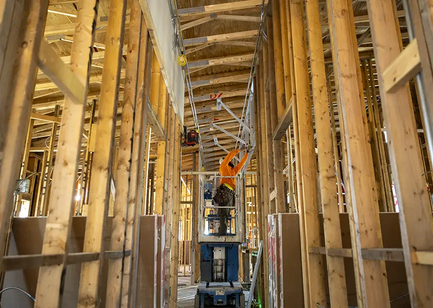 A construction worker stands in the middle of an interior building renovation that features wooden beams.