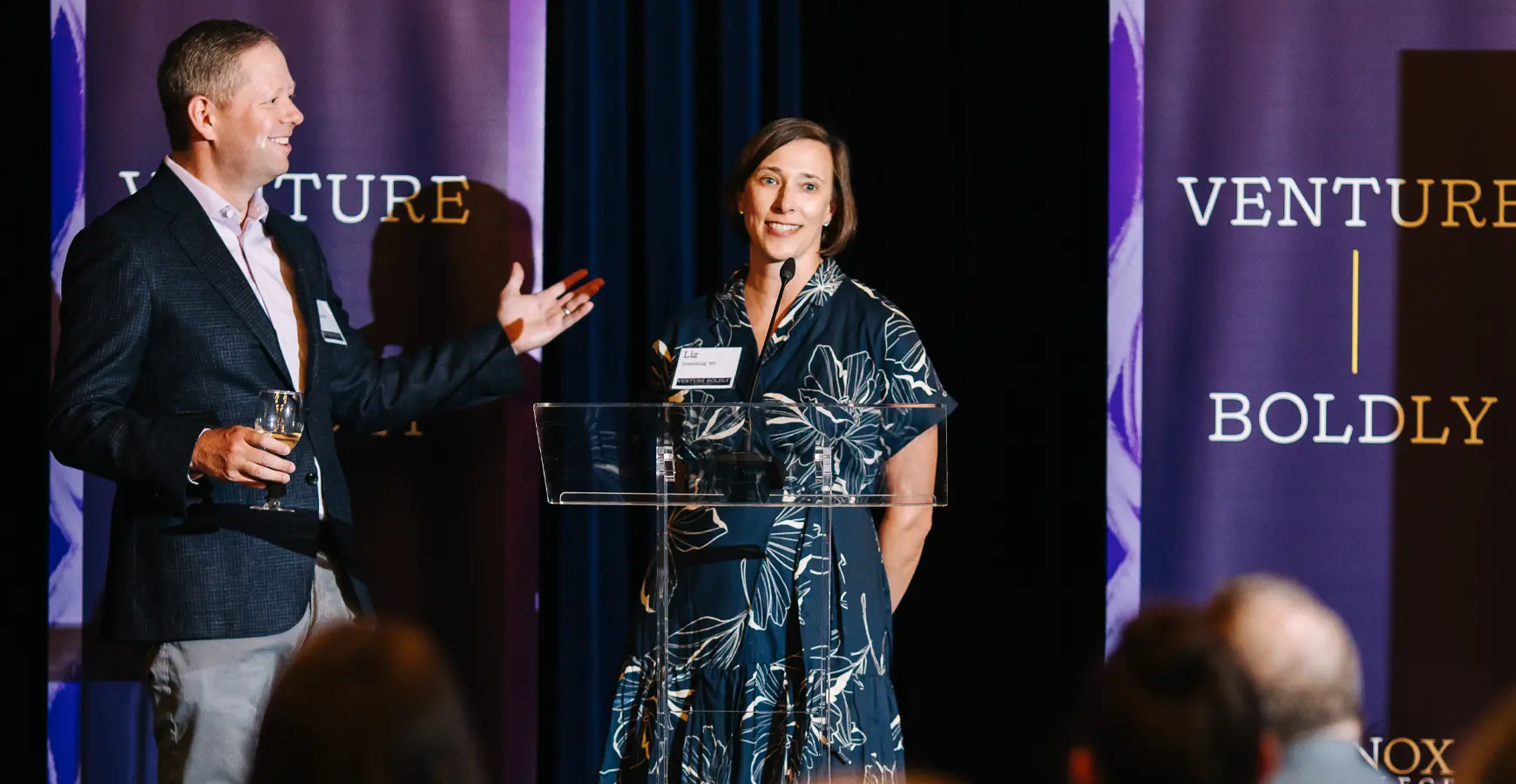 Dan and Liz Spaulding, both Knox Class of 1999, at a podium in front of the banner that says Venture Boldly.