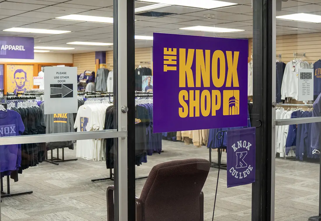 The Knox Shop Campus Store is shown through its window. Apparel on clothing racks can be seen in the background.