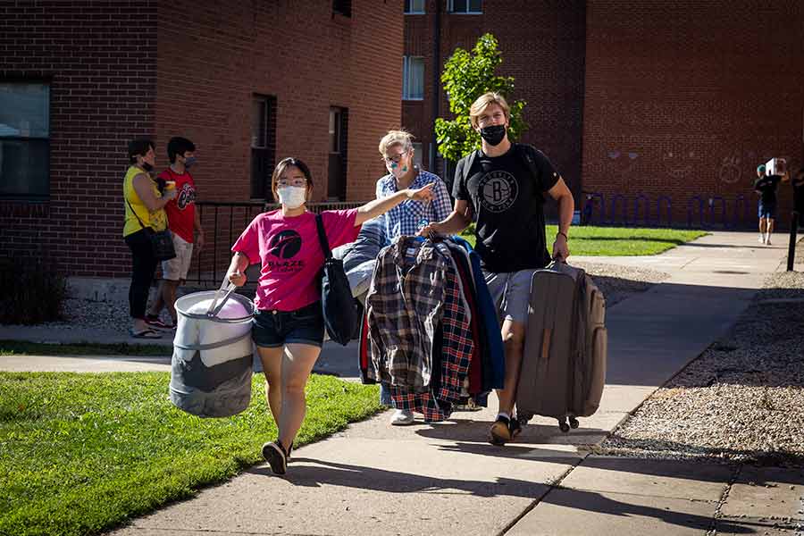 A student in a pink shirt guides newly arrived students on a sidewalk as they carry luggage and move onto the Knox campusesident McGadney to campus.
