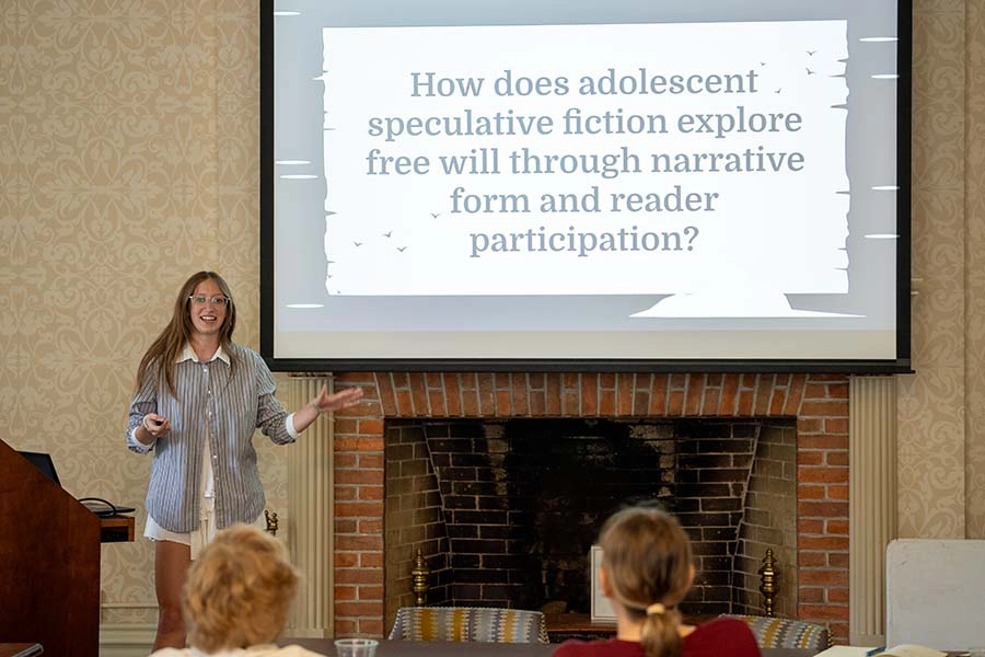 A Knox student stands by a podium at the front of a room presenting her summer research. 