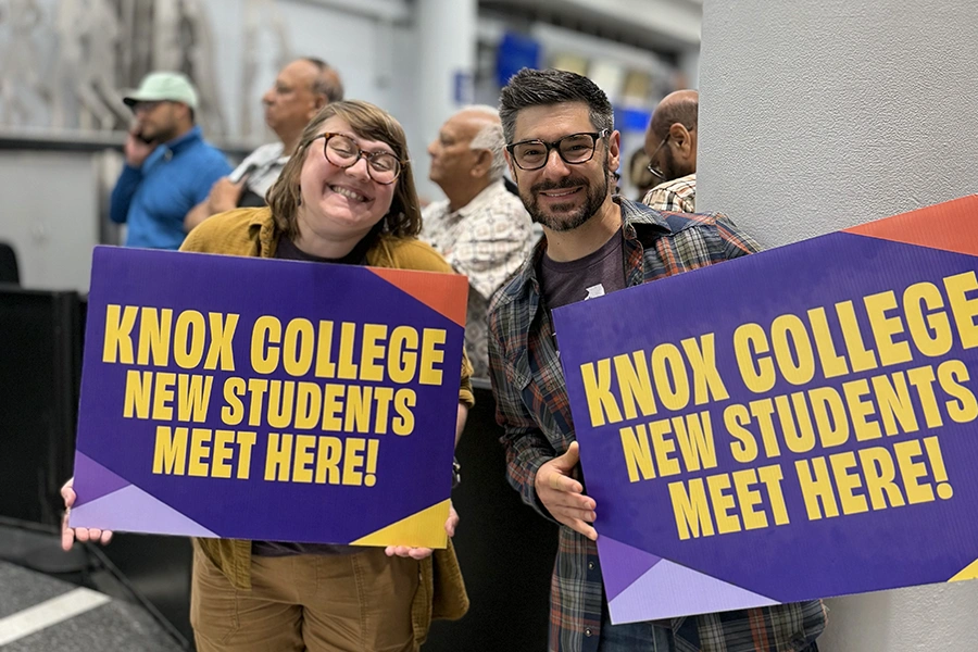 Two Knox Admissions Counselors smile, holding signs that say Knox College New Students Meet Here!