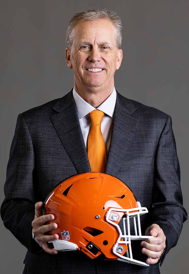 Todd Monken in a suit and orange tie holding an orange helmet.