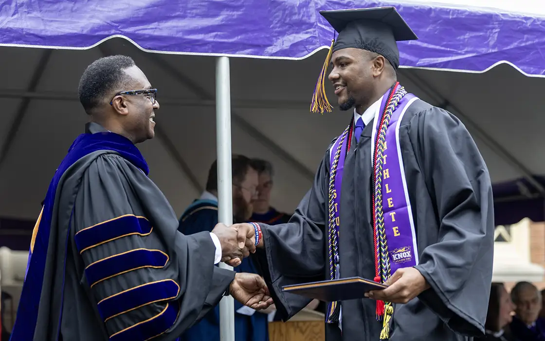 President McGadney shakes hands with a graduate as the graduate receives his diploma. 