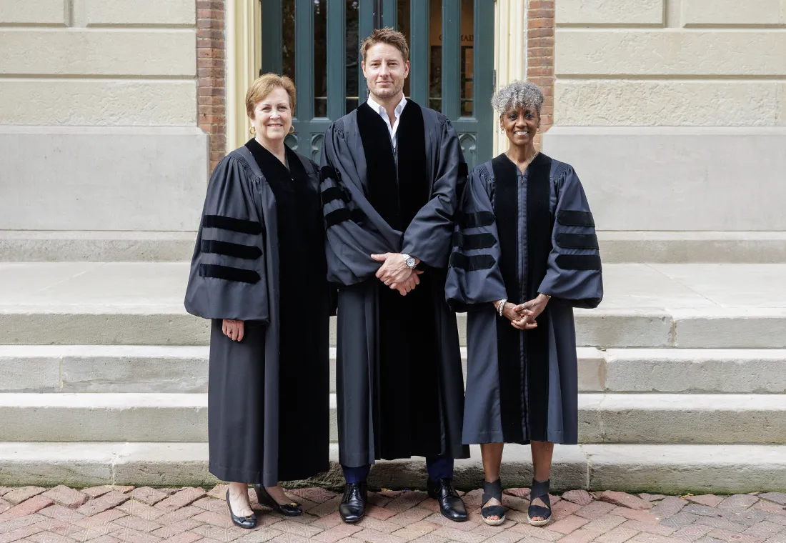 Deborah F. Rutter, Justin Hartley, and Dorothy Tucker stand together in academic regalia in front of the steps of Old Main. 