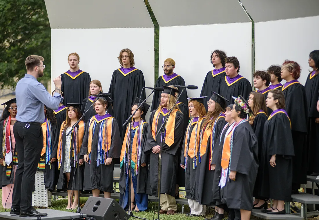 The Knox College Choir stands on risers, singing as they are directed by the choir director. 