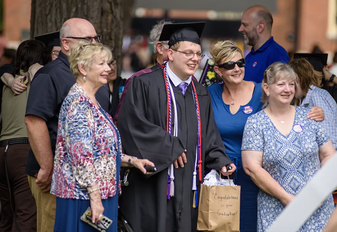 A graduate smiles, surrounded by his family. He holds a gift bag that says Congratulations on your Graduation. 