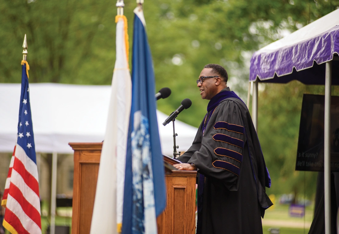 President McGadney, dressed in academic regalia, stands behind a podium on a stage and speaks.