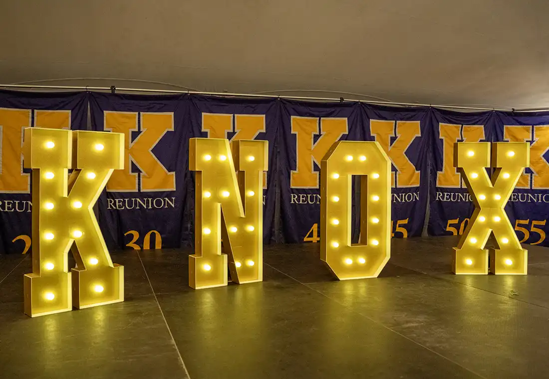 A lit up sign that spells Knox sits in front of seven flags with Reunion years printed on them.