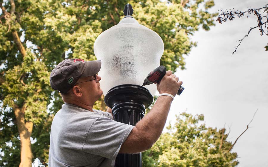Knox College electrician installs an energy-saving LED bulb in the globe on a campus light pole.
