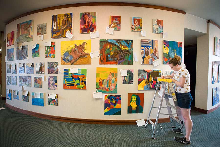 Student Kristen Marvin mounts paintings, records entry info, for the 2018 Al Young Art Show.