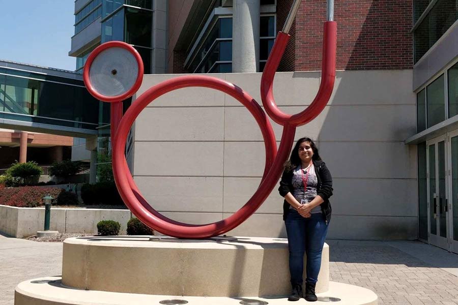 Neha stands by sculpture of stethoscope.