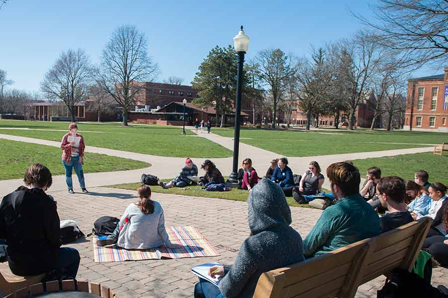 A student reads from Homer's The Odyssey as other students watch. 