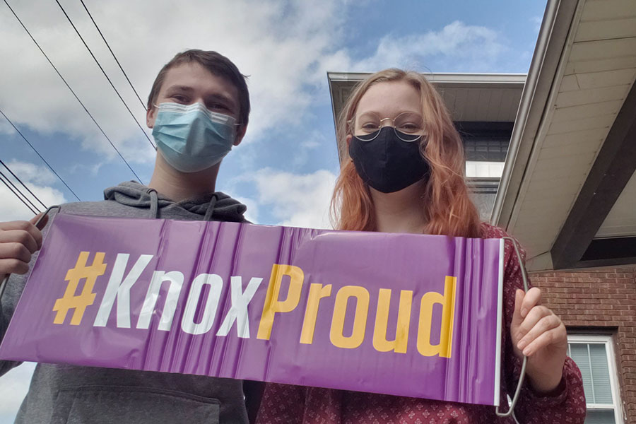 Two students in face masks brandish a purple banner reading "#KnoxProud."