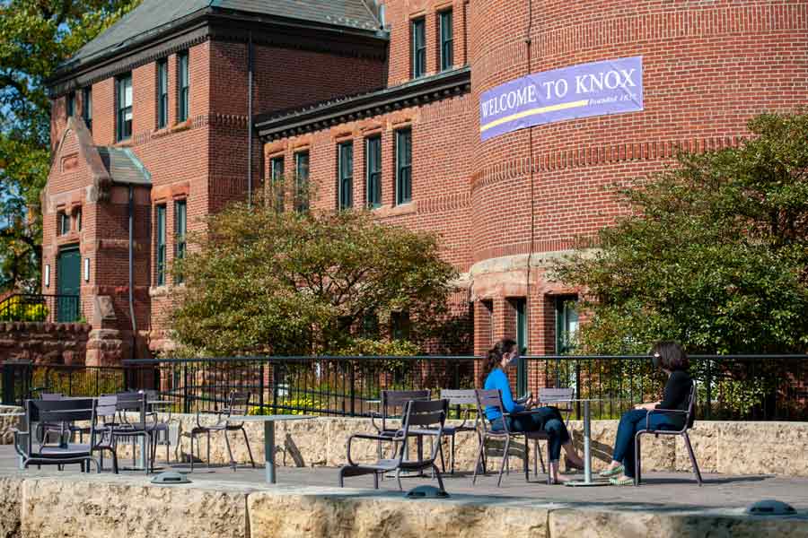 Students take a break by talking and sitting at a table on Plomin Terrace, the patio outside of Alumni Hall.