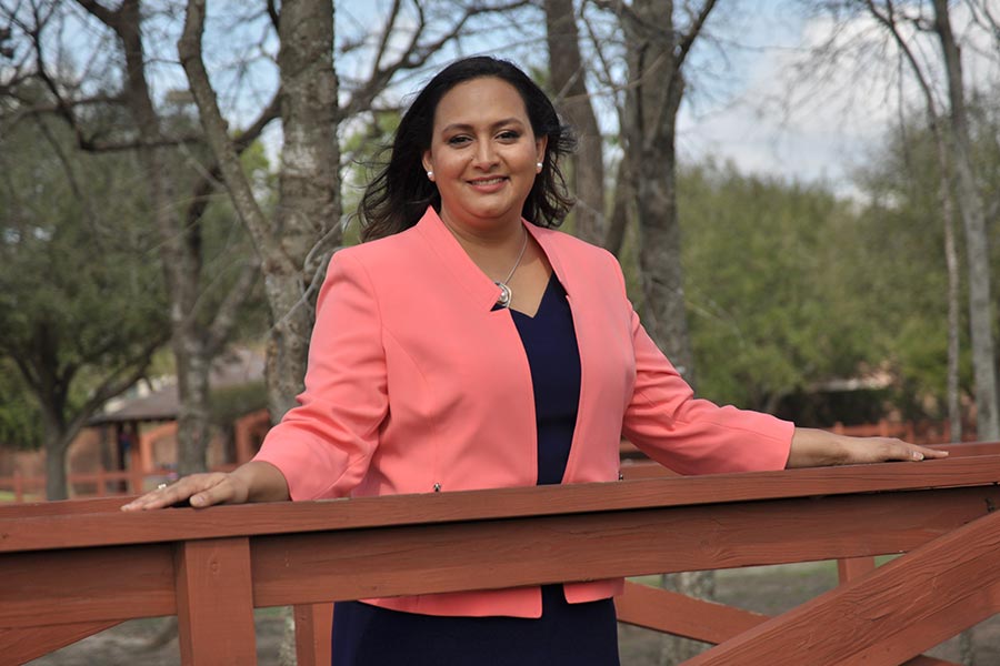 Pamela Hernandez leans against a railing outside, with trees in the background