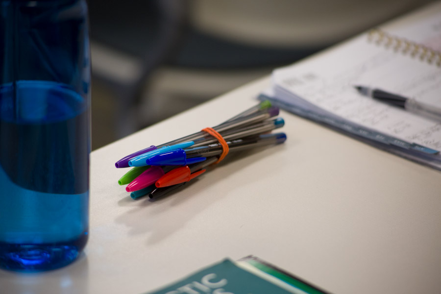 Pens, paper, water bottle on a desk. 