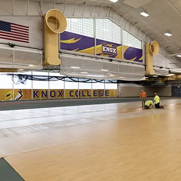 Workers install a basketball court surface as part of the T. Fleming Fieldhouse resurfacing project.