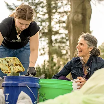 Two individuals work over bins, sorting waste. 