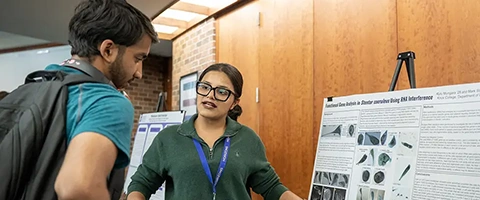A student points to a poster on an easel as she speaks to another student.