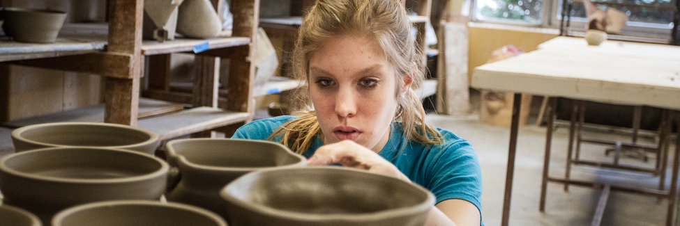 A student checks clay bowls as they dry in the ceramics studio.